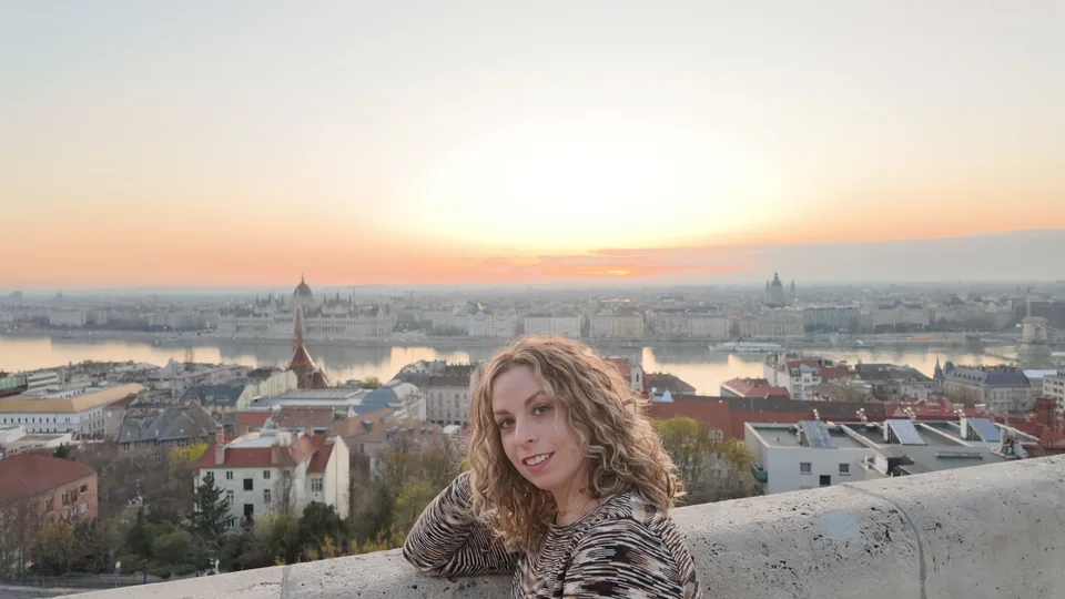 A smiling person beside a stone railing overlooking a city and river