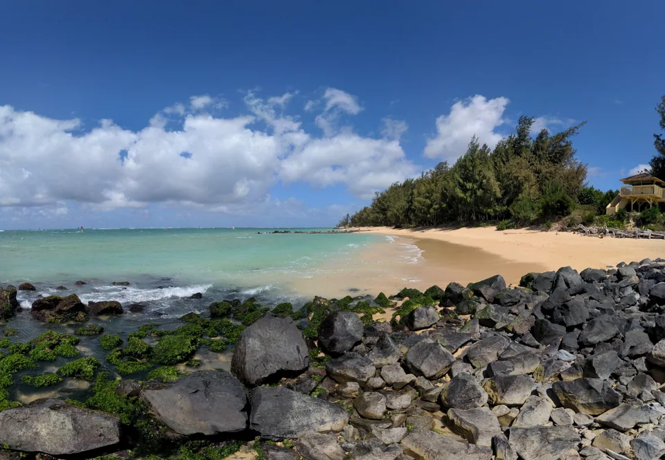 Turquoise water beside a sandy beach and dark coastal rocks