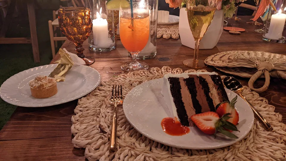 A slice of cake, glasses and place settings on a candlelit table